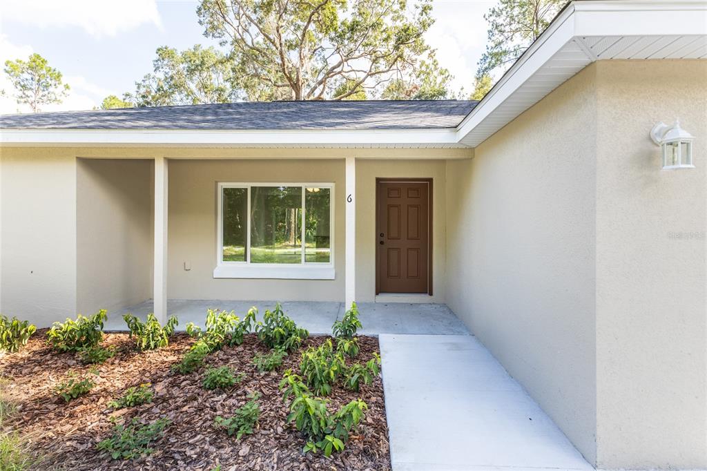 The exterior of a single-story house features a brown front door, a window, and landscaping — 1057 NW TIMBERLAKE ROAD, DUNNELLON, FL