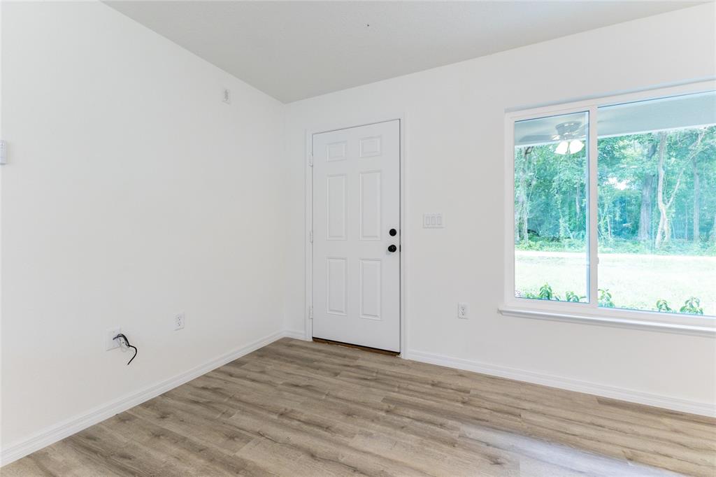 An empty room features white walls, wood-look flooring, a white door, and a large window — 1057 NW TIMBERLAKE ROAD, DUNNELLON, FL