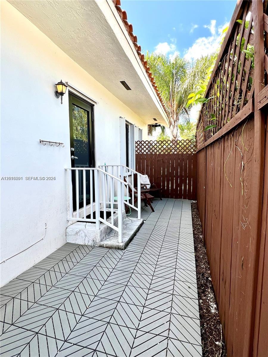 A narrow outdoor patio features gray patterned flooring, a white railing, and a wooden fence — MIAMI, FL