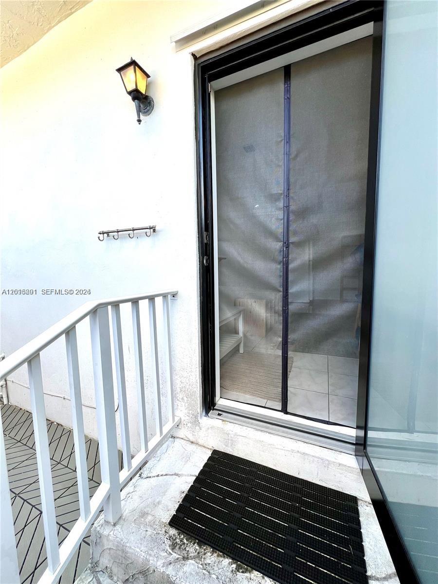 A balcony features a white railing, a black door screen, and a black rubber mat — MIAMI, FL