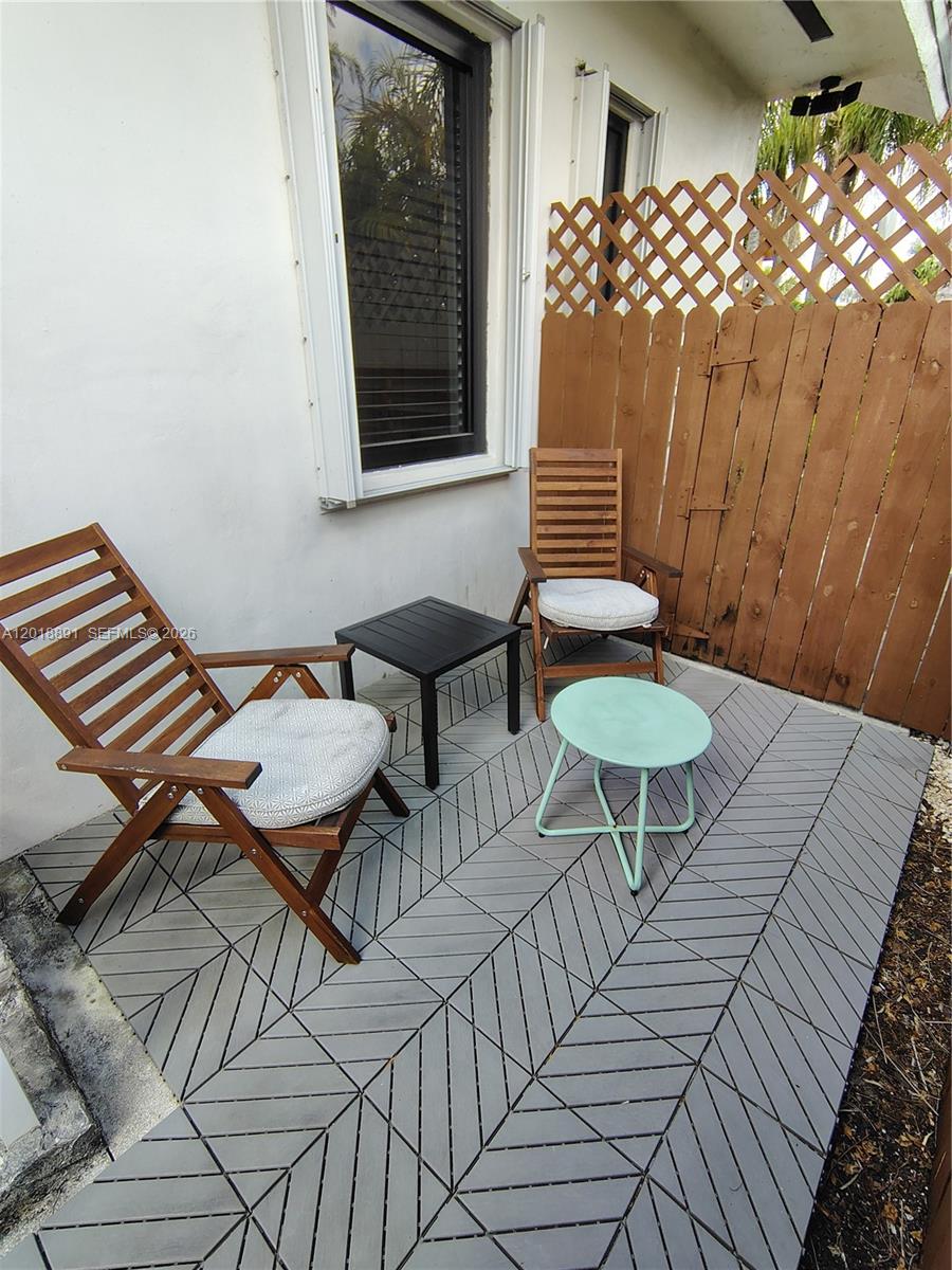 A small outdoor patio features two wooden chairs, two side tables, and gray interlocking tiles — MIAMI, FL