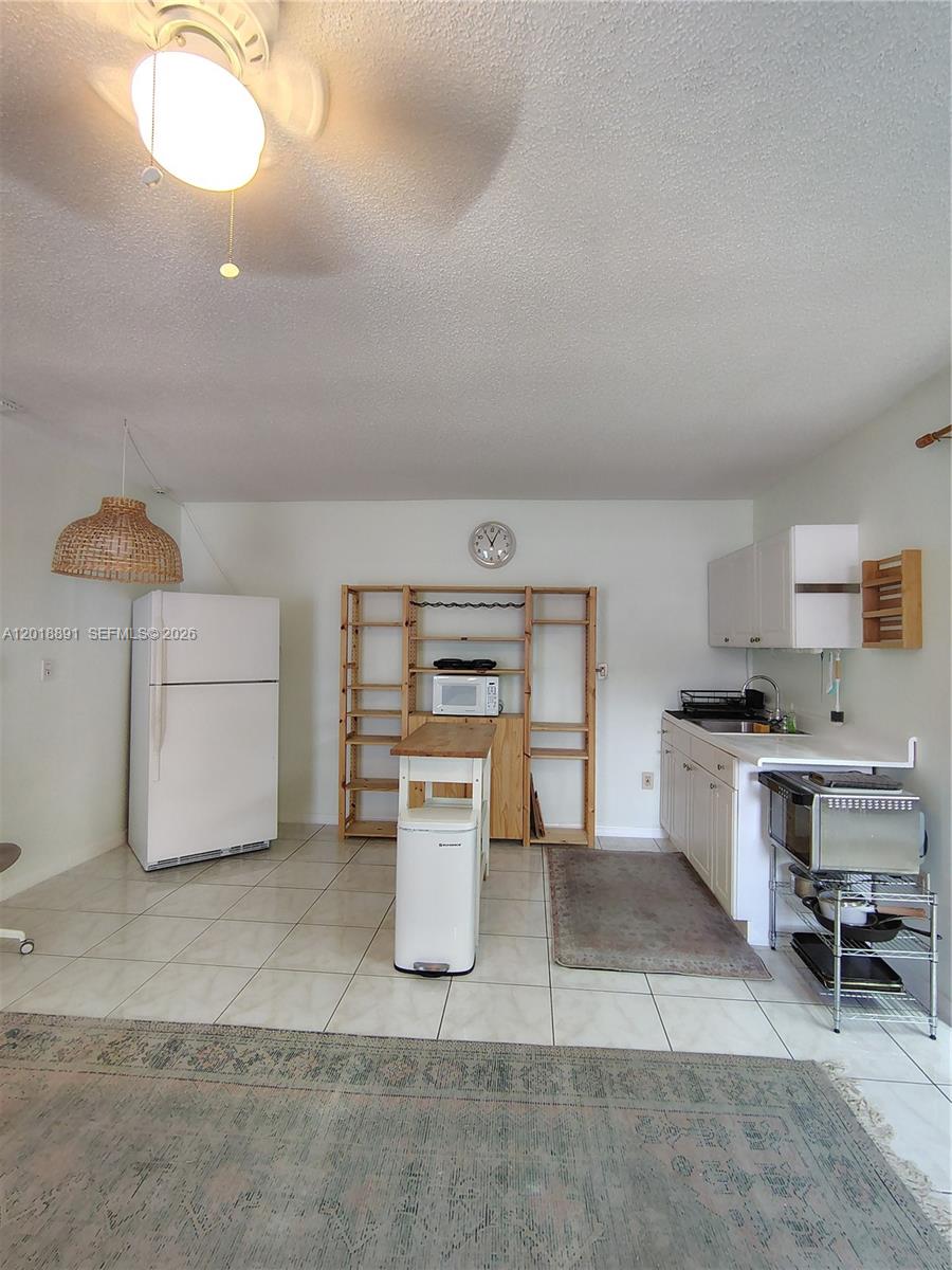 This kitchen features white cabinets, a refrigerator, a wooden shelving unit, and tiled flooring — MIAMI, FL