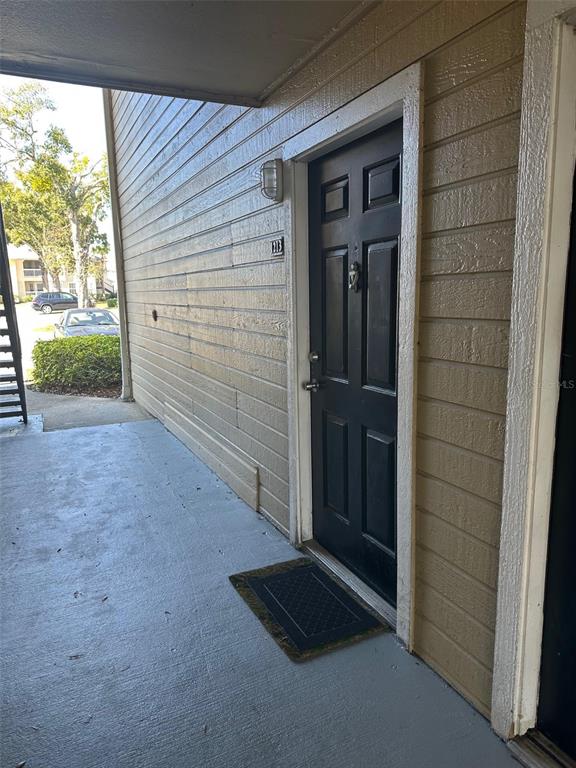 A black front door with a door knocker is set into a tan wood-sided exterior wall — 1071 S HIAWASSEE ROAD UNIT 1213, ORLANDO, FL