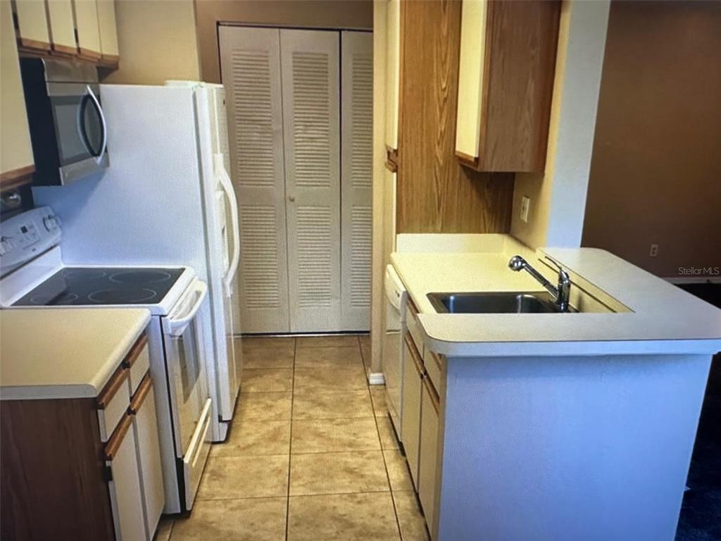 A kitchen features white appliances, wood-trimmed cabinets, a tiled floor, and a sink in the counter — 1071 S HIAWASSEE ROAD UNIT 1213, ORLANDO, FL