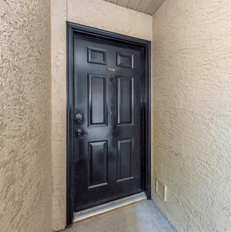 A black six-panel front door with a digital lock is set in a stucco wall — 2400 FEATHER SOUND DRIVE UNIT 412, CLEARWATER, FL