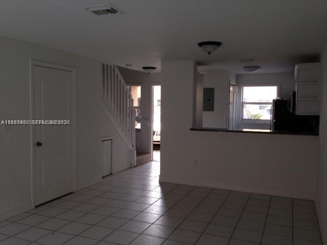 A room with white tiled floors, a staircase, and an opening to a kitchen area — 7905 NW 8 ST # 8A, Miami FL 33126, MIAMI, FL
