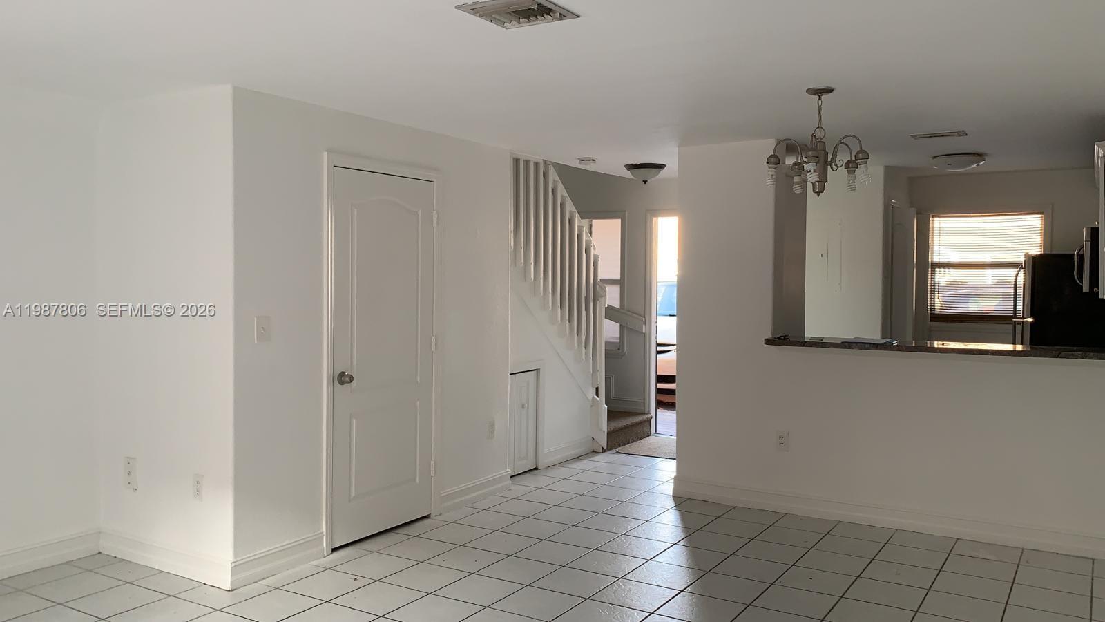 A white-walled room features a tiled floor, a staircase, and a kitchen pass-through window — 7905 NW 8 ST # 8A, Miami FL 33126, MIAMI, FL