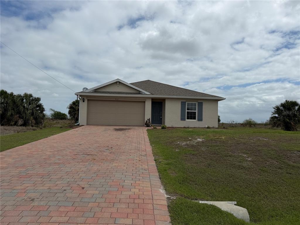 A single-story house with a beige exterior, a brick paver driveway, and a two-car garage — 513 ELLA JEAN PI, BANYAN VILLAGE, LABELLE, FL