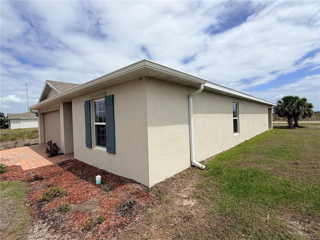 The exterior of a beige stucco house features a garage, blue shutters, and a downspout — 513 ELLA JEAN PI, BANYAN VILLAGE, LABELLE, FL