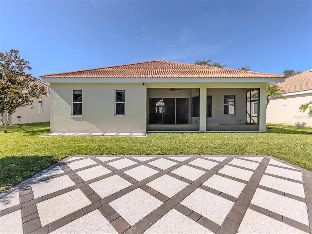 The rear exterior of a house features a screened-in lanai and a geometric paver patio — 6511 WESTWARD PLACE, BRADENTON, FL