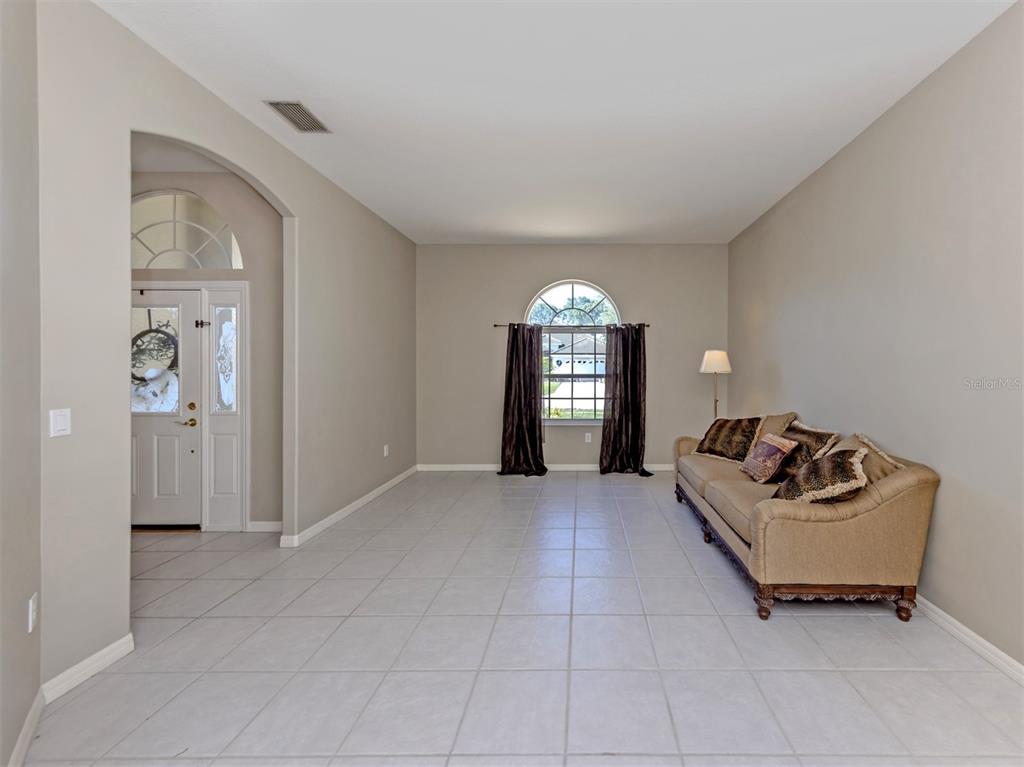 A living room features light tile flooring, beige walls, an arched window, and a tan sofa — 6511 WESTWARD PLACE, BRADENTON, FL