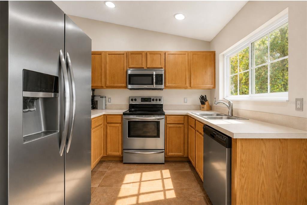 A kitchen with stainless steel appliances, oak cabinets, and a window above the sink — 2830 OSPREY COVE PLACE UNIT 203, KISSIMMEE, FL