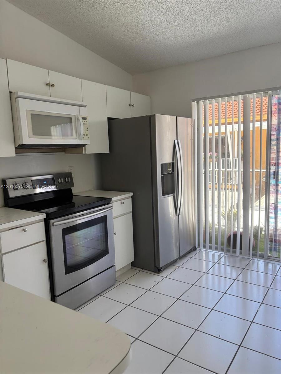 A kitchen features white cabinets, stainless steel appliances, and white tile flooring near a sliding door — 7778 W 34th Ln # 201, Hialeah FL 33018, HIALEAH, FL