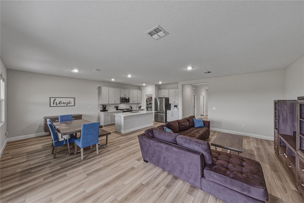 An open-concept living room and kitchen area featuring light wood flooring and a sectional sofa — 12253 CATTLESIDE DRIVE, RIVERVIEW, FL