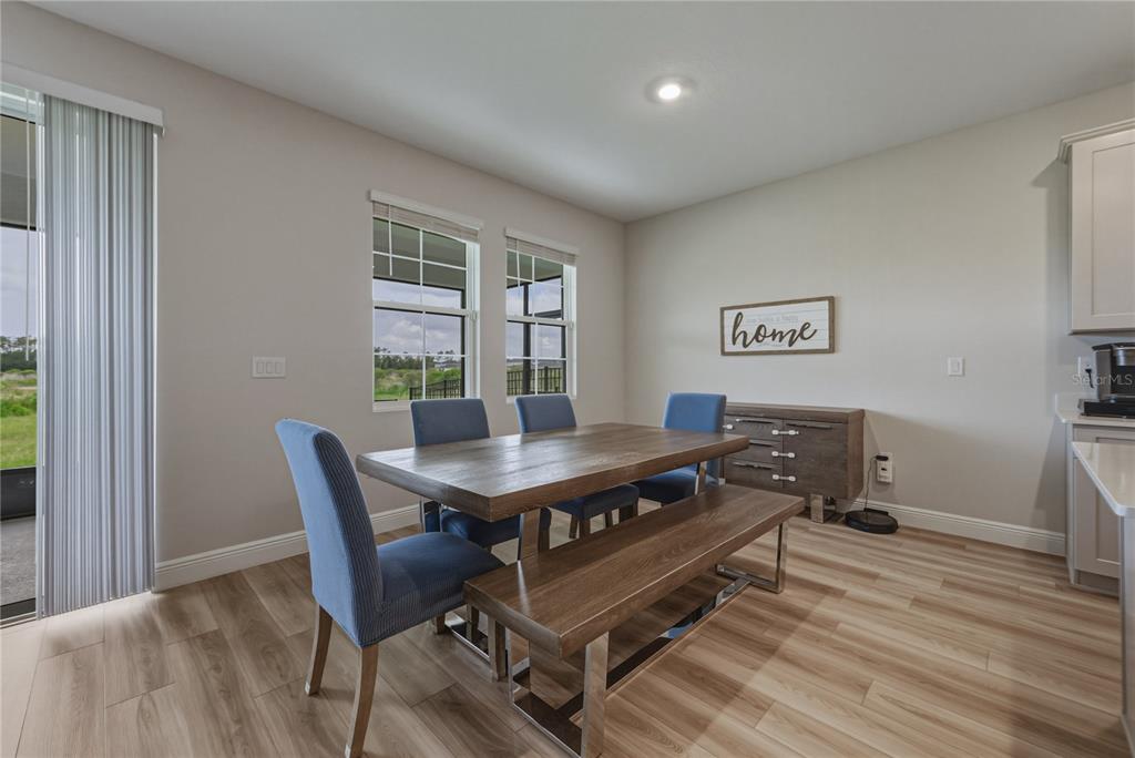 A dining area features a wooden table, blue chairs, a bench, and light wood-look flooring — 12253 CATTLESIDE DRIVE, RIVERVIEW, FL
