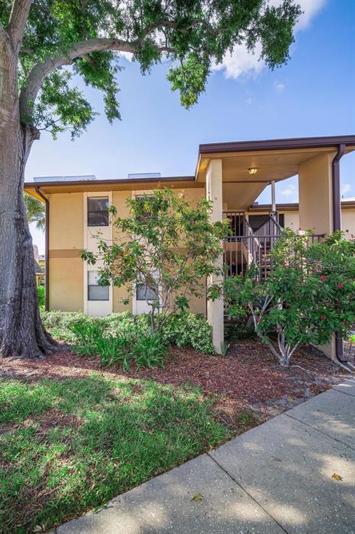 A two-story apartment building exterior features a covered staircase, tan stucco walls, and landscaping — 10195 SAILWINDS BOULEVARD N UNIT 201, LARGO, FL