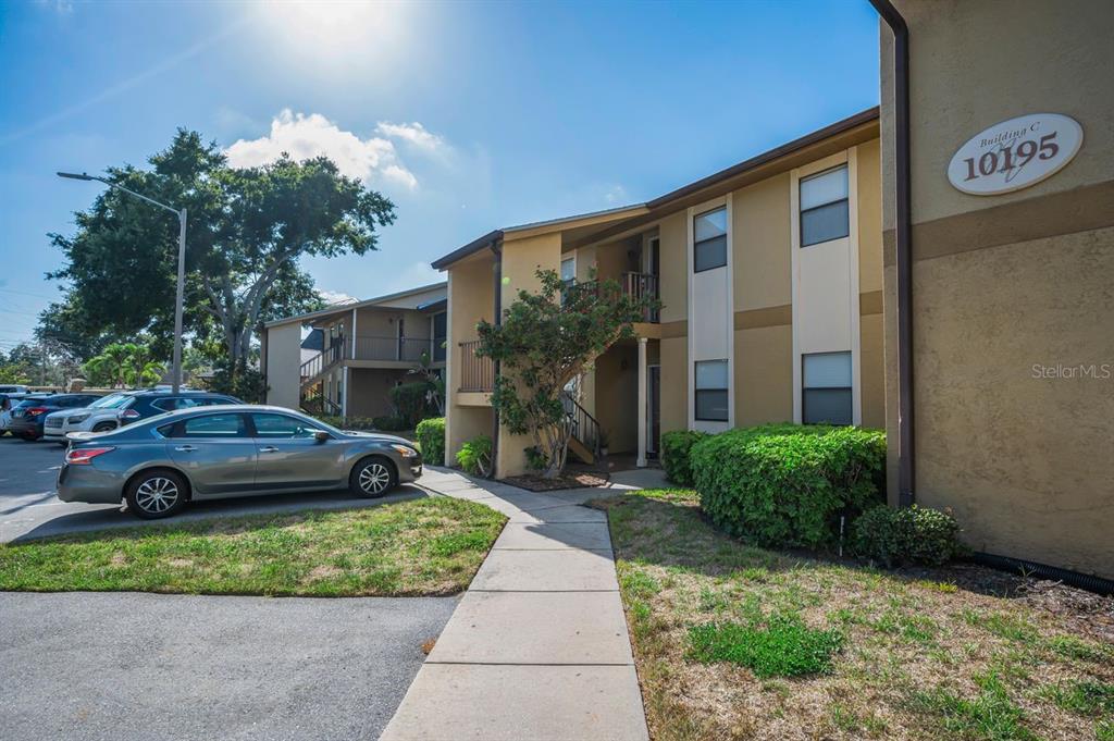 A multi-story apartment building exterior with a sidewalk, parking lot, and a parked car — 10195 SAILWINDS BOULEVARD N UNIT 201, LARGO, FL