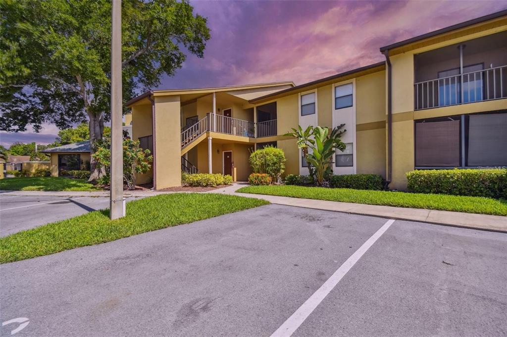 A two-story apartment building with tan stucco walls, screened balconies, and a parking lot — 10195 SAILWINDS BOULEVARD N UNIT 201, LARGO, FL