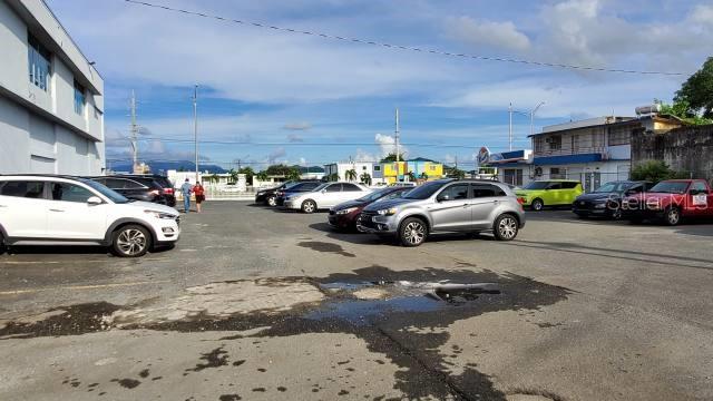 A paved parking lot with several parked cars sits in front of a commercial building — 1 PR-1 INT. SAKURA ST., CAGUAS, PR