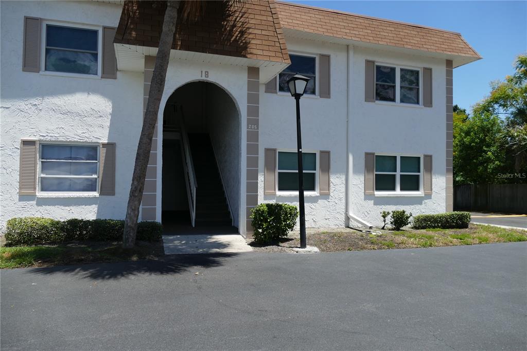 A two-story apartment building exterior features a white stucco facade, brown roof, and arched entryway — 205 S MCMULLEN BOOTH ROAD UNIT 203, CLEARWATER, FL