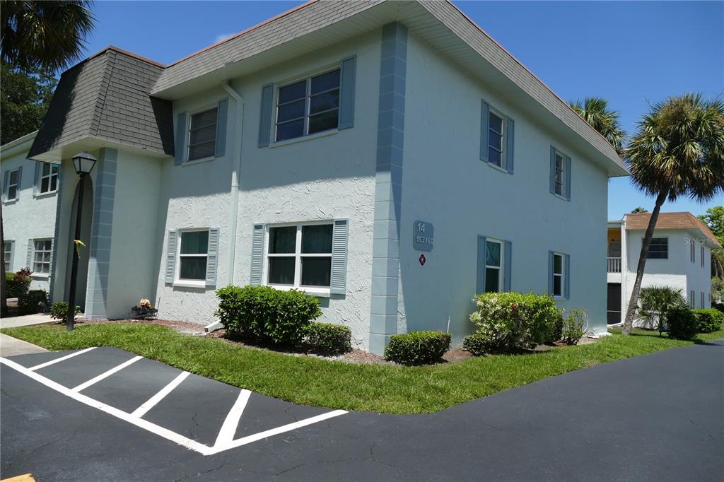 A two-story apartment building with light-colored stucco walls, blue shutters, and a parking lot — 205 S MCMULLEN BOOTH ROAD UNIT 203, CLEARWATER, FL