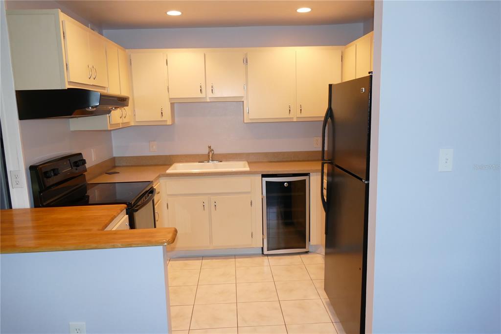 A kitchen with white cabinets, black appliances, a wine cooler, and light-colored tile flooring — 205 S MCMULLEN BOOTH ROAD UNIT 203, CLEARWATER, FL