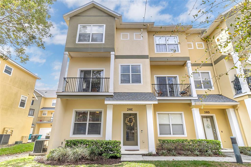 The exterior of a three-story yellow townhouse features balconies, white trim, and a front entrance — 28 W ESTHER STREET UNIT E, ORLANDO, FL