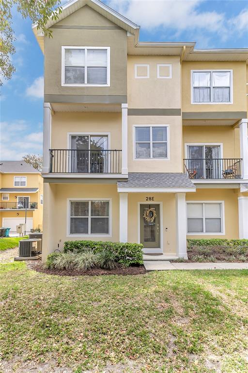 A three-story townhouse with a tan stucco exterior, a front balcony, and a covered entrance — 28 W ESTHER STREET UNIT E, ORLANDO, FL
