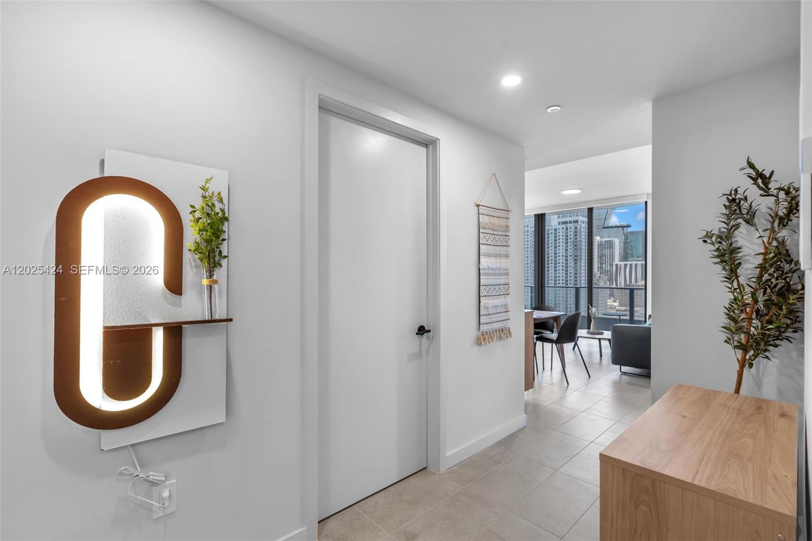 A hallway with a lighted wall sculpture leads to a living area with city views — 121 NE 5th St # 2301, Miami FL 33132, MIAMI, FL