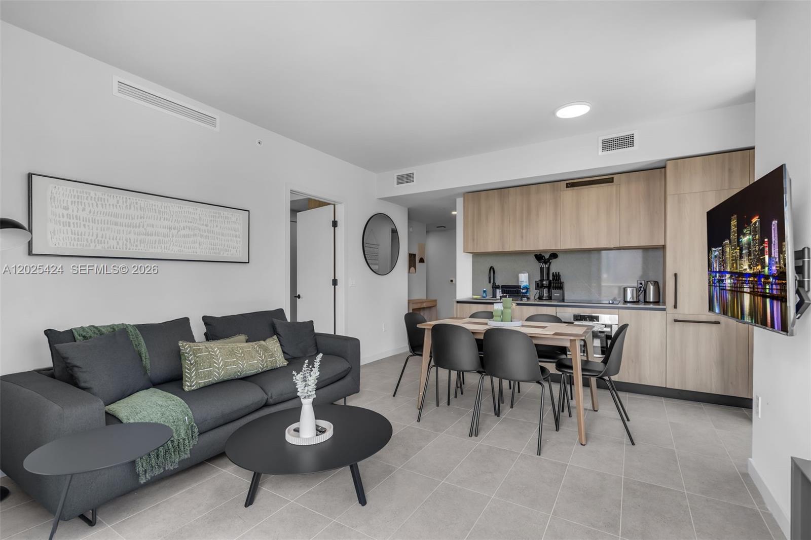 A modern open-plan living and dining area features a grey sofa and light wood cabinetry — 121 NE 5th St # 2301, Miami FL 33132, MIAMI, FL