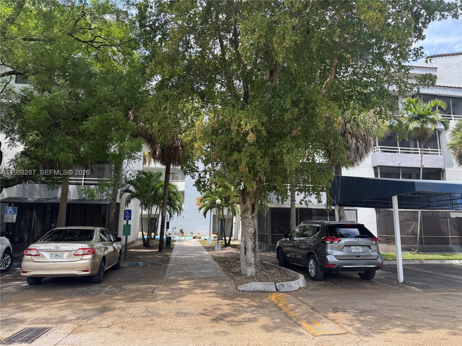 A paved walkway leads between two residential buildings with parked cars and mature trees — 8305 SW 152nd Ave # 201, Miami FL 33193, MIAMI, FL