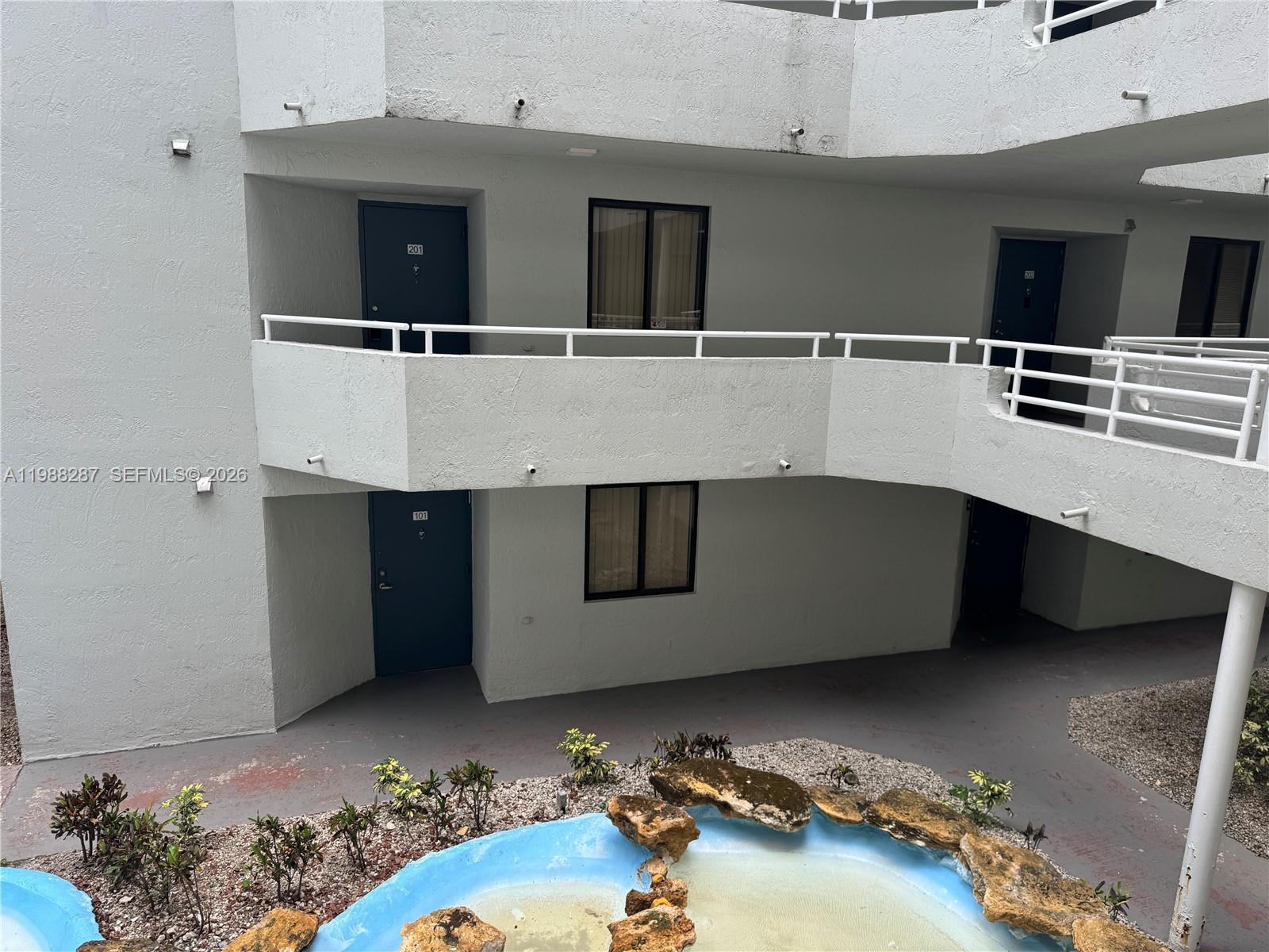 An exterior view shows apartment building balconies overlooking a small, decorative stone-lined pond — 8305 SW 152nd Ave # 201, Miami FL 33193, MIAMI, FL