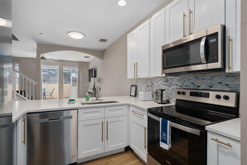 A kitchen features white cabinets, stainless steel appliances, a quartz countertop, and a tiled backsplash — 1204 S BEACH CIR, KISSIMMEE, FL