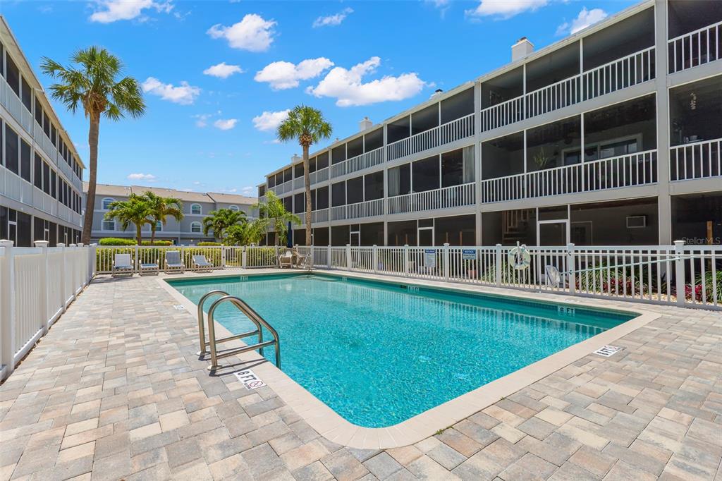A rectangular swimming pool sits in a paved courtyard surrounded by multi-story apartment buildings — 737 PINELLAS BAYWAY S UNIT 308, ST PETERSBURG, FL