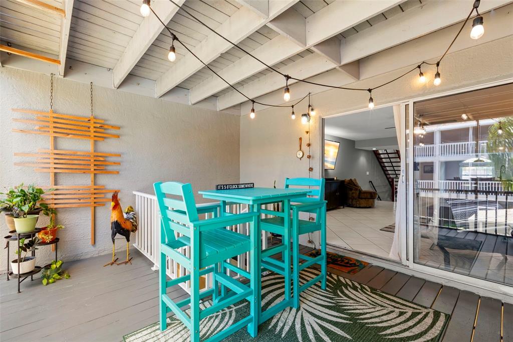 A covered patio features a turquoise bistro set, string lights, and a decorative rooster statue — 737 PINELLAS BAYWAY S UNIT 308, ST PETERSBURG, FL