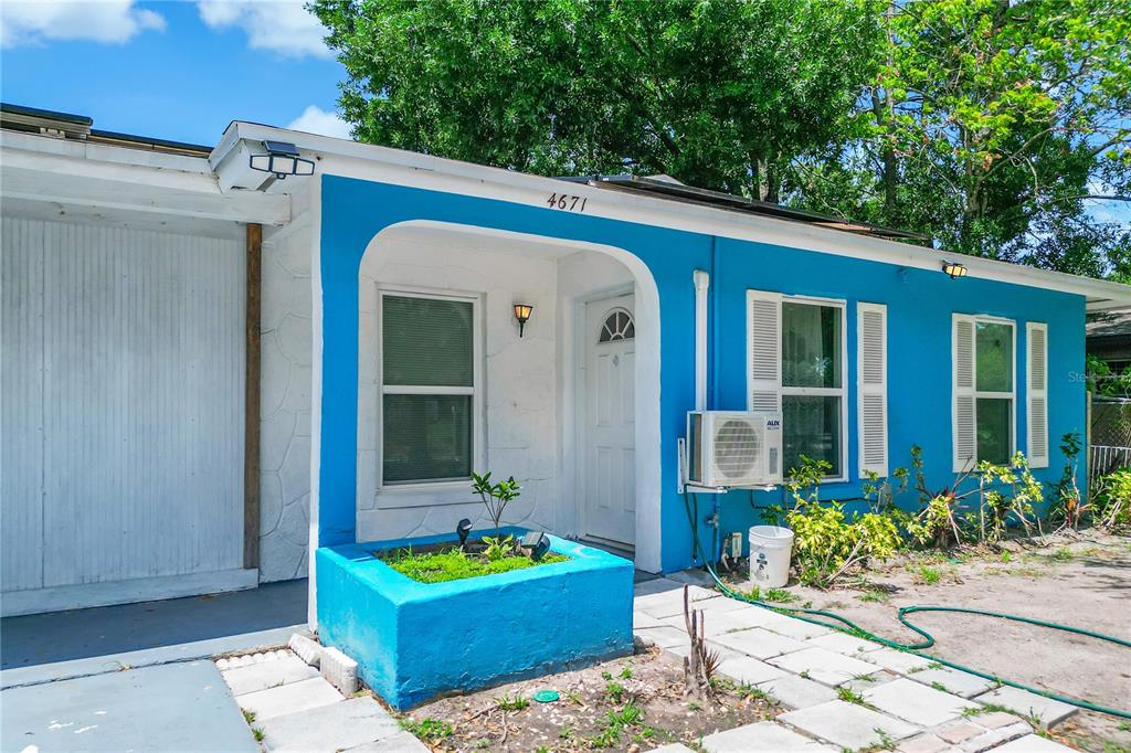 A bright blue exterior house features a white front door and a raised garden bed — 4671 VERGARA COURT, ORLANDO, FL