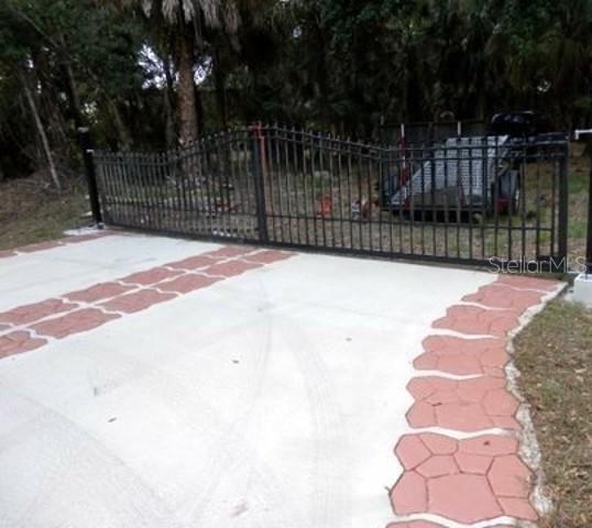 A black metal gate stands at the entrance of a concrete driveway with decorative borders — 17314 WELLSLEY AVENUE, PORT CHARLOTTE, FL