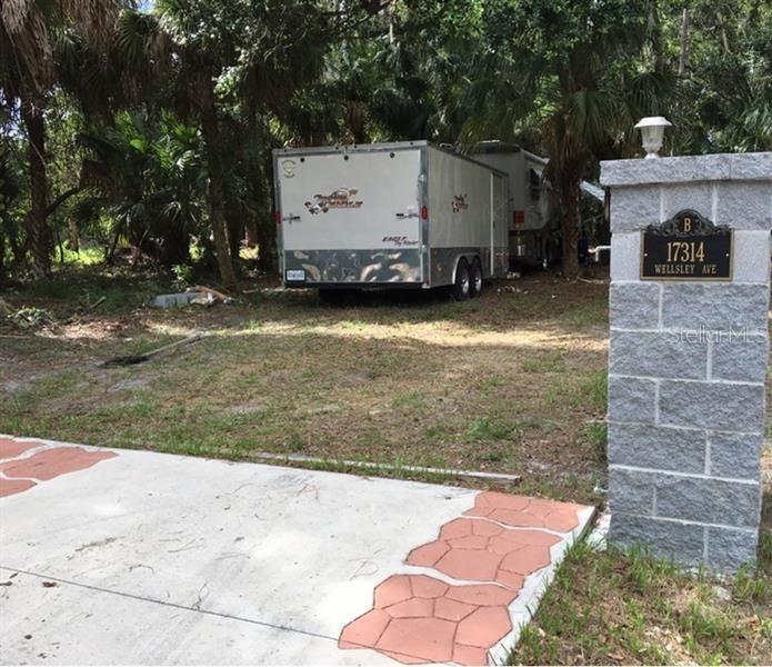 A trailer and a motorhome are parked on a wooded lot behind a stone pillar — 17314 WELLSLEY AVENUE, PORT CHARLOTTE, FL