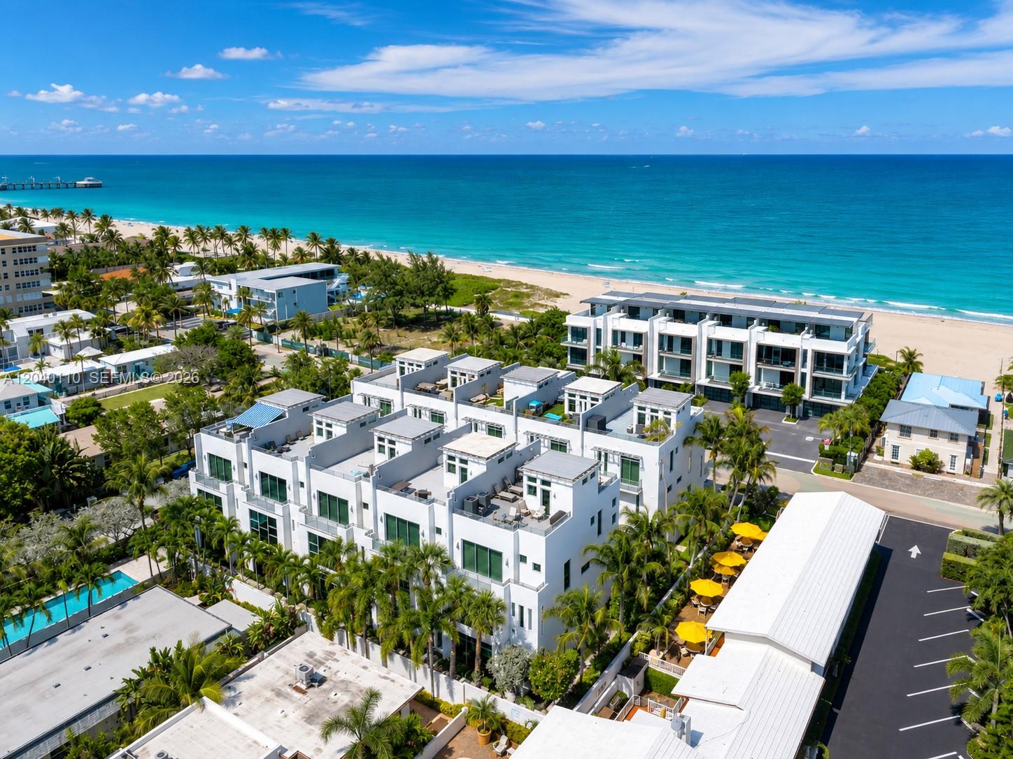 An aerial view shows modern white townhouses near a beach with palm trees and ocean — 3406 SE 6th St # 3406, Pompano Beach FL 33062, POMPANO BEACH, FL