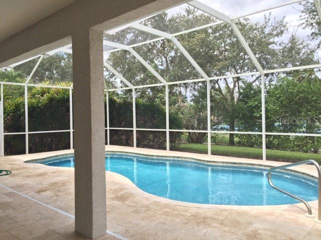 A screened-in swimming pool with a stone patio sits under a white metal enclosure — 17947 COURTSIDE LANDINGS CIRCLE, PUNTA GORDA, FL