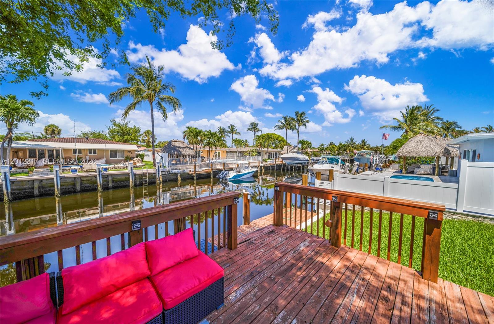 A wooden deck with red cushions overlooks a canal lined with boats and palm trees — 31 SE 12th St, Pompano Beach FL 33060, POMPANO BEACH, FL