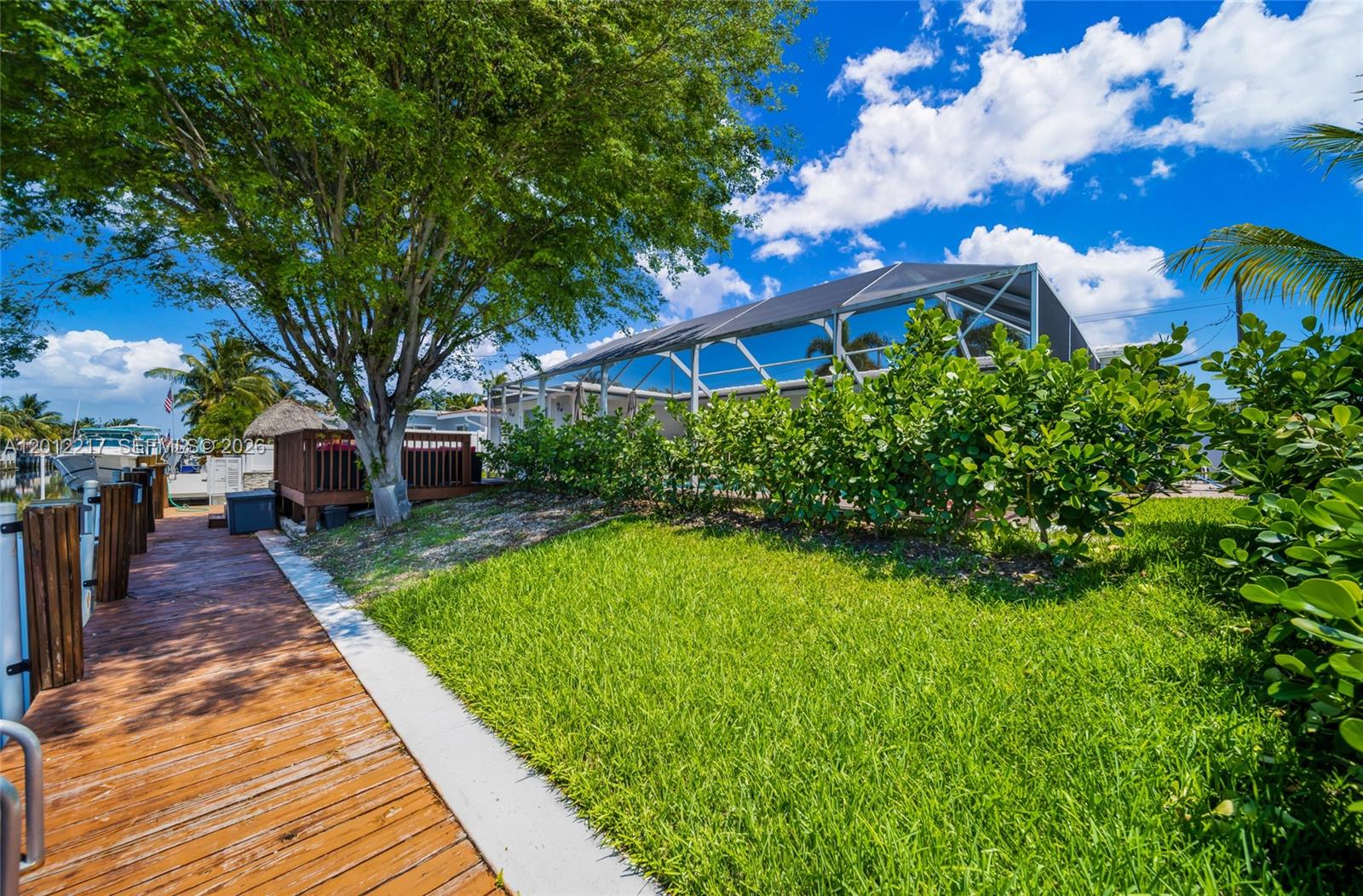 A wooden dock leads to a grassy yard with a screened-in pool enclosure and trees — 31 SE 12th St, Pompano Beach FL 33060, POMPANO BEACH, FL