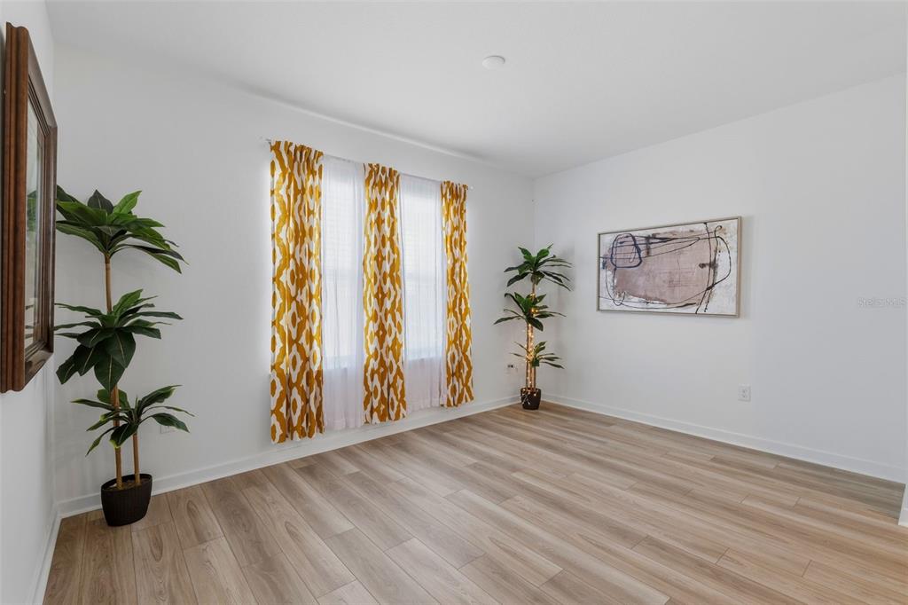 An empty room features light wood-look flooring, white walls, yellow patterned curtains, and two plants — 10517 HIDDEN BANKS GLEN, PARRISH, FL