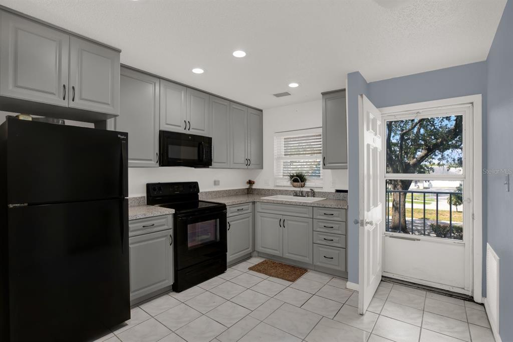 A kitchen with grey cabinets, black appliances, speckled countertops, and a door leading outside — 4939 FLORAMAR TERRACE UNIT 204, NEW PORT RICHEY, FL