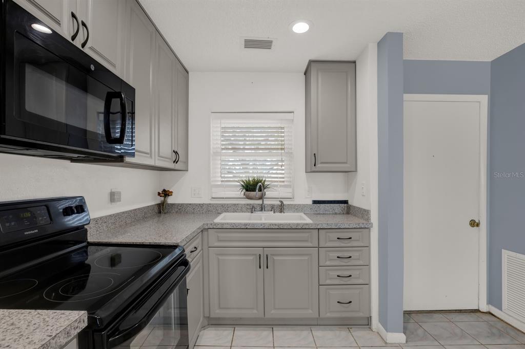A kitchen features gray cabinets, speckled granite countertops, a white sink, and black appliances — 4939 FLORAMAR TERRACE UNIT 204, NEW PORT RICHEY, FL