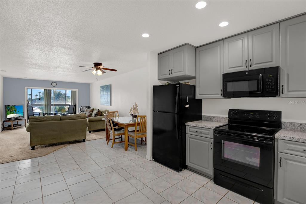 A kitchen with grey cabinets and black appliances opens into a living and dining area — 4939 FLORAMAR TERRACE UNIT 204, NEW PORT RICHEY, FL