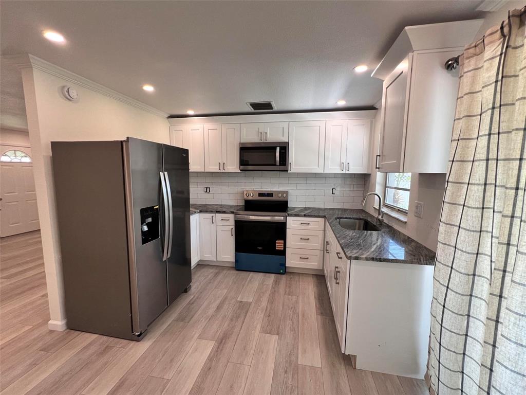 A kitchen features white cabinets, stainless steel appliances, granite countertops, and light wood-look flooring — 3339 VAN NUYS LOOP, NEW PORT RICHEY, FL