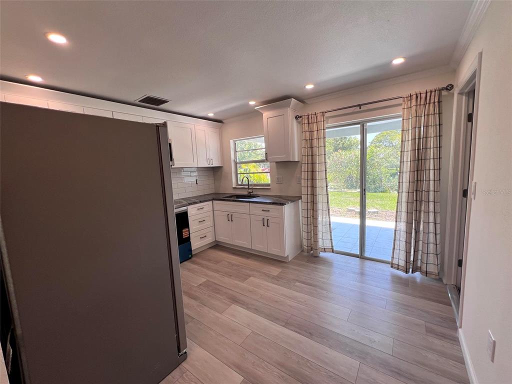 A kitchen features white cabinets, dark countertops, light wood-look flooring, and a sliding glass door — 3339 VAN NUYS LOOP, NEW PORT RICHEY, FL