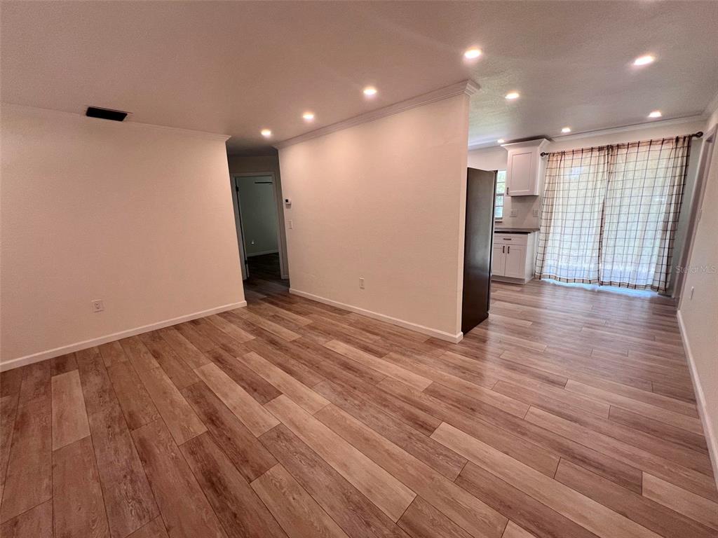 A living area with wood-look flooring leads to a kitchen and sliding glass doors — 3339 VAN NUYS LOOP, NEW PORT RICHEY, FL