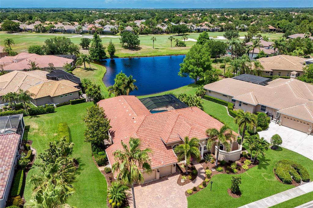 An aerial view of a suburban house with a tile roof, pool cage, and pond — 7207 ASHLAND GLEN, LAKEWOOD RANCH, FL
